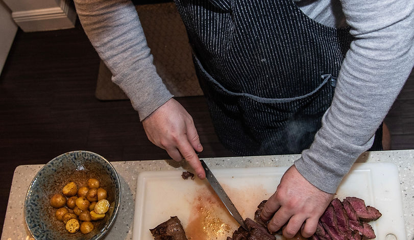 Chef slicing steak overhead with roasted potatoes