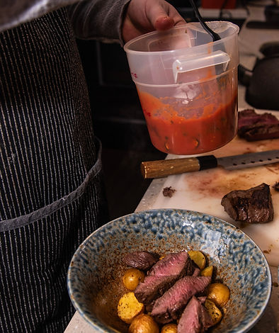 Chef plating sliced steak with roasted potatoes and red sauce